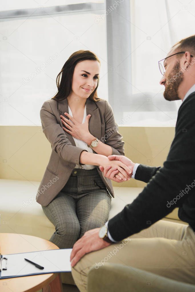 smiling patient and psychologist shaking hands in doctors office