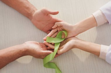 partial view of male and female hands with green ribbon - mental health day clipart