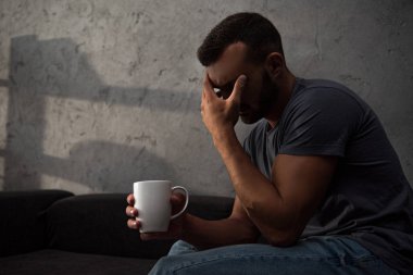 lonely crying man holding cup of coffee sitting at home clipart