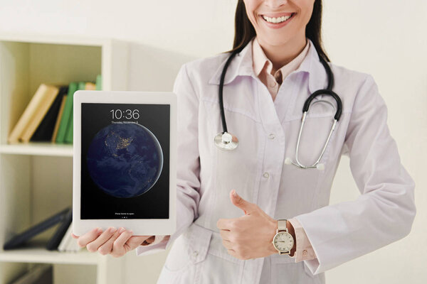 cropped view of doctor showing thumb up and presenting ipad