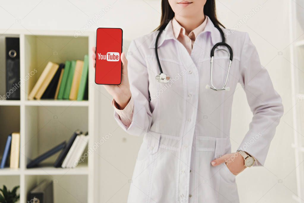 Cropped view of doctor with stethoscope showing smartphone with youtube app