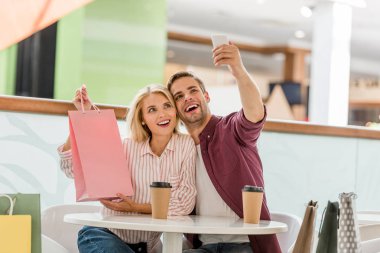 adam alışveriş çantası masada tek kullanımlık bardak kahve Cafe ile gösterilen kız arkadaşı ile selfie alarak 