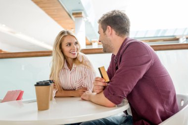 Genç adam kız arkadaşına masada kafede kahve fincanı ile konuşurken kredi kartıyla gülümseyen 