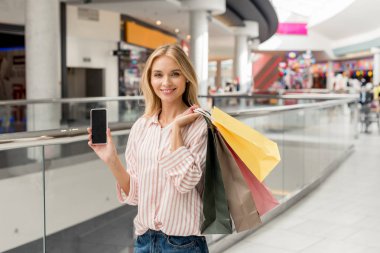 Alışveriş merkezinde smartphone boş ekran ile gösterilen kağıt poşet olan mutlu kadın 