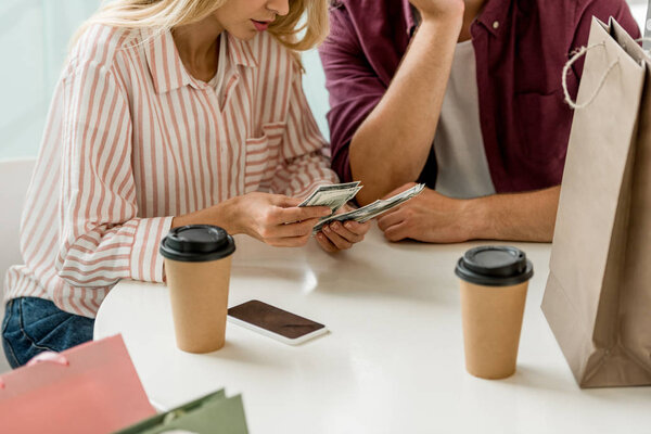 partial view of young couple counting cash money at table with coffee cups in cafe 