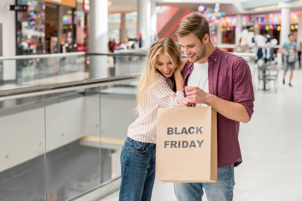 年轻夫妇的购物者向下看和手持纸袋黑色星期五在购物中心 — 图库照片