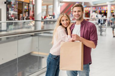 alışveriş alışveriş merkezi kameraya bakarak kese kağıdı ile mutlu genç çift 