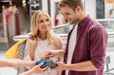 Genç adam kız arkadaşı alışveriş merkezinde alışveriş torbaları ile yakın ayakta iken terminal üzerindeki kredi kartıyla ödeme 