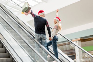 Dikiz alışveriş Noel şapka kaldırdı kollarını kağıtları torbaları yürüyen merdiven üzerinde tutarak içinde birkaç 