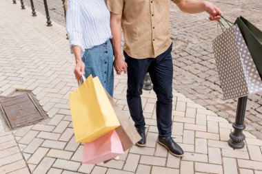 cropped image of stylish couple of shoppers with paper bags standing on street clipart