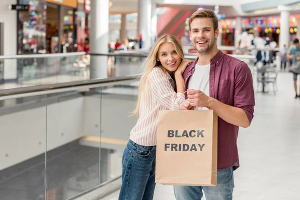 快乐的年轻夫妇持有纸袋与字体黑色星期五在购物中心 — 图库照片