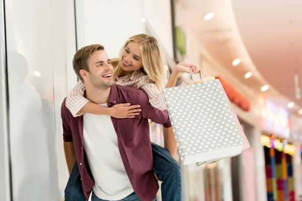 若い男がモールで買い物袋のガール フレンドに与えるおんぶ — ストック写真
