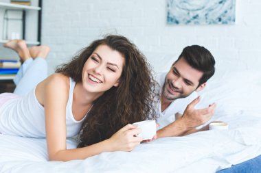 mutlu genç çift bardak kahve basılı tutup yatağa gülüyor