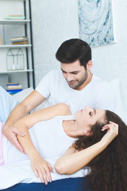 yatakta uyuyan güzel kız arkadaşı bakarak gülümseyen yakışıklı genç