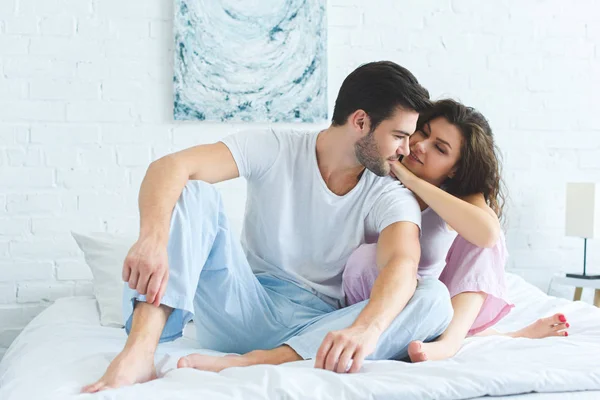 パジャマを着てベッドに一緒に座っている若いカップルの笑顔が美しい — ストック写真