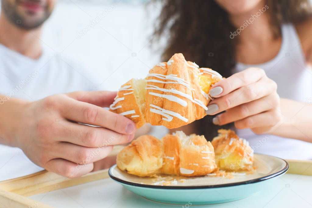 close-up view of young couple sharing croissant for breakfast
