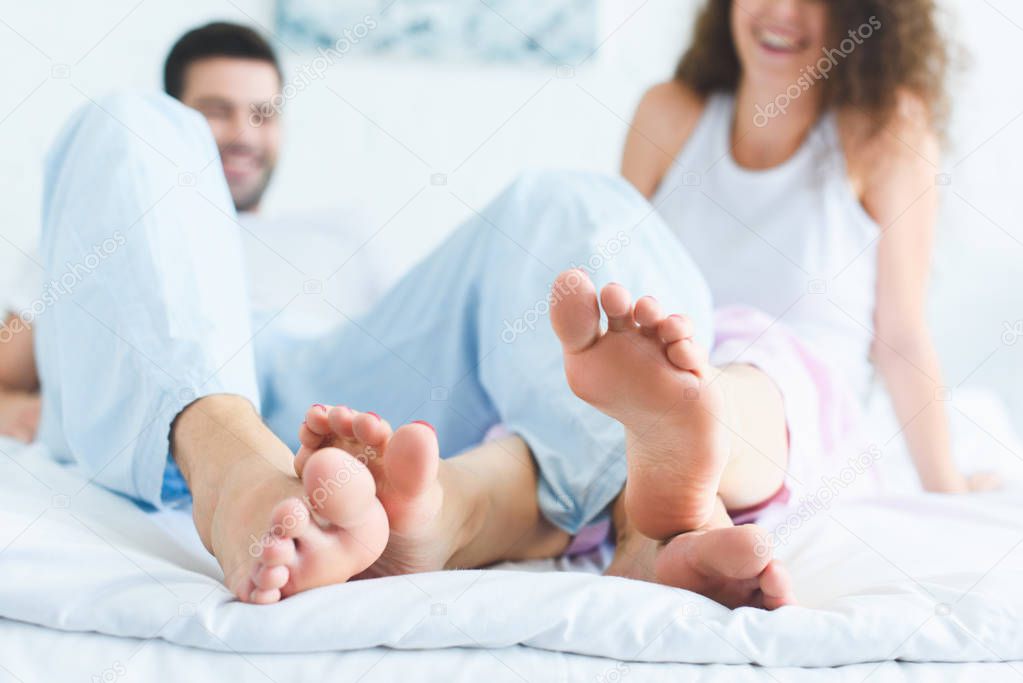 close-up view of feet of happy young couple on bed at morning