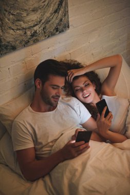 mutlu genç çiftin akıllı telefonlar geceleri yatakta kullanarak yüksek açılı görünüş