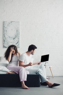 dizüstü bilgisayar ile boş ekran, ilişki zorluklar kavramı kullanarak kızgın adam yatakta oturan genç kadın