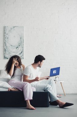 Yatağa kızgın adam facebook Web sitesinde ekran ile dizüstü bilgisayar kullanarak oturan genç kadın