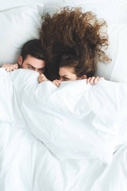 genç çiftin birbirine yatakta beyaz battaniye altında yalan süre bakarak üstten görünüm  