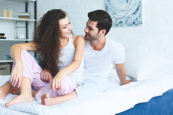 パジャマを着てベッドに座って お互いに笑みを浮かべて美しい幸せな若いカップル — ストック写真