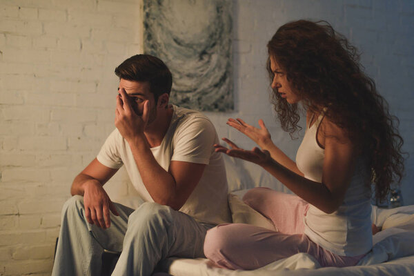 emotional young woman quarreling with upset boyfriend on bed, relationship difficulties concept