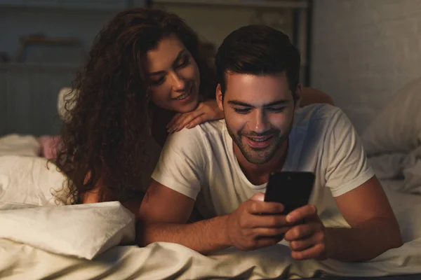 Feliz Jovem Casal Deitado Cama Usando Smartphone Juntos — Fotografia de Stock