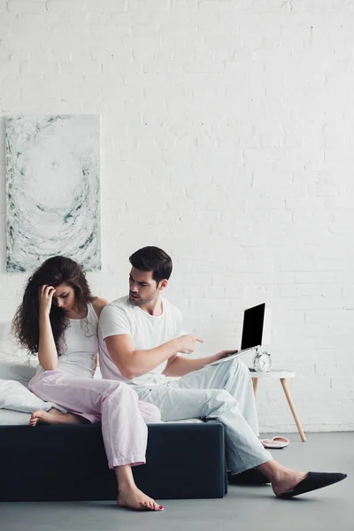 Upset Young Woman Sitting Bed While Man Pointing Finger Laptop — Free Stock Photo