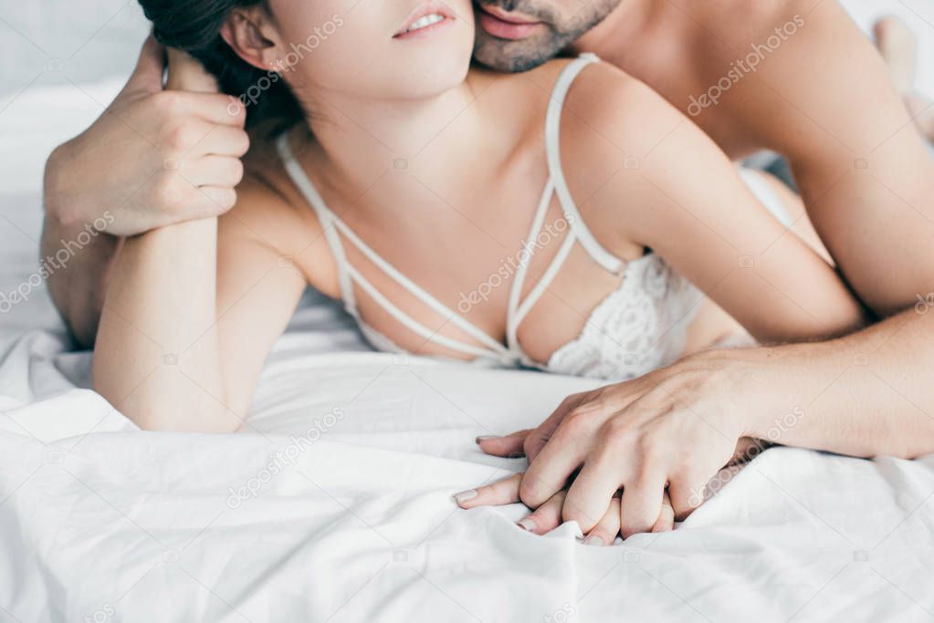 cropped shot of sexy young couple holding hands in foreplay on bed