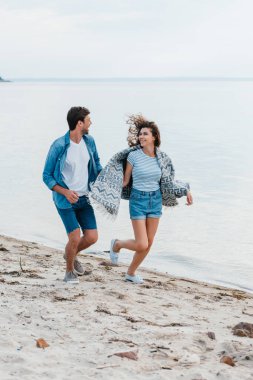 Genç çift tutuşup gülümseyen ve sahil üzerinde çalışan