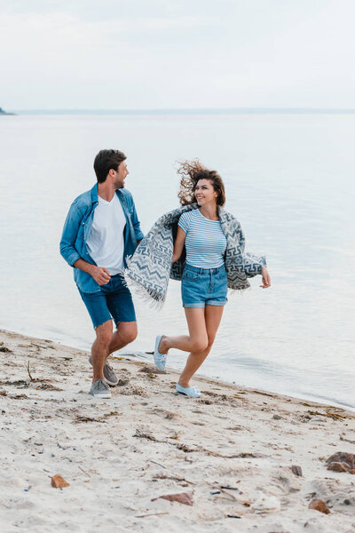 young smiling couple holding hands and running on seashore