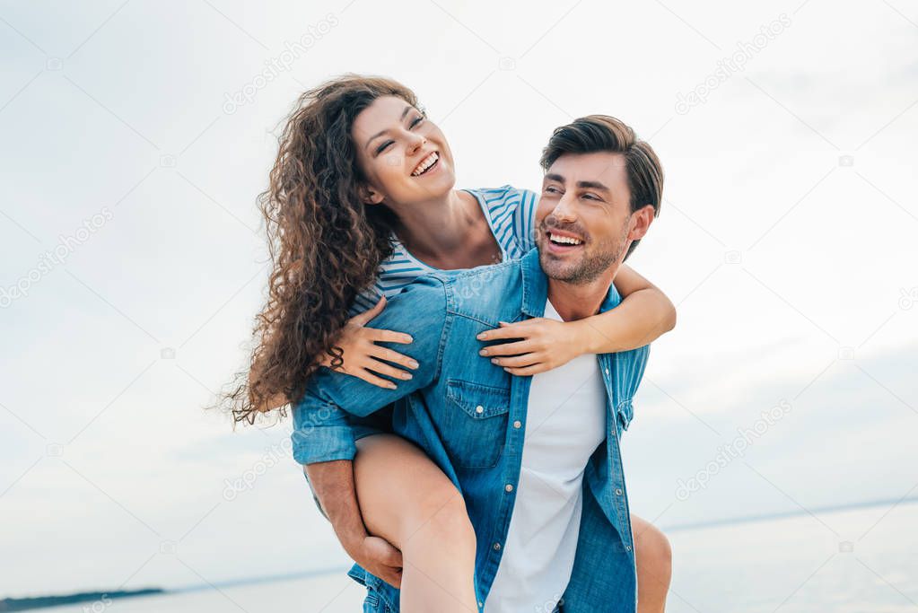 happy couple having fun and piggybacking near sea 