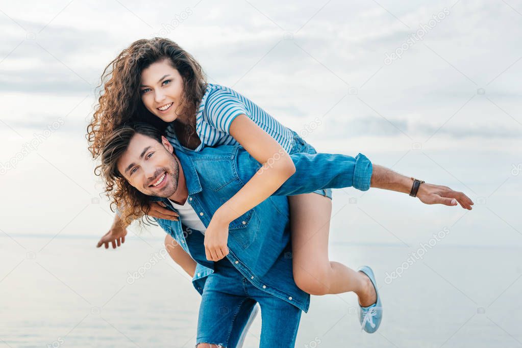 smiling boyfriend piggybacking his girlfriend on seashore