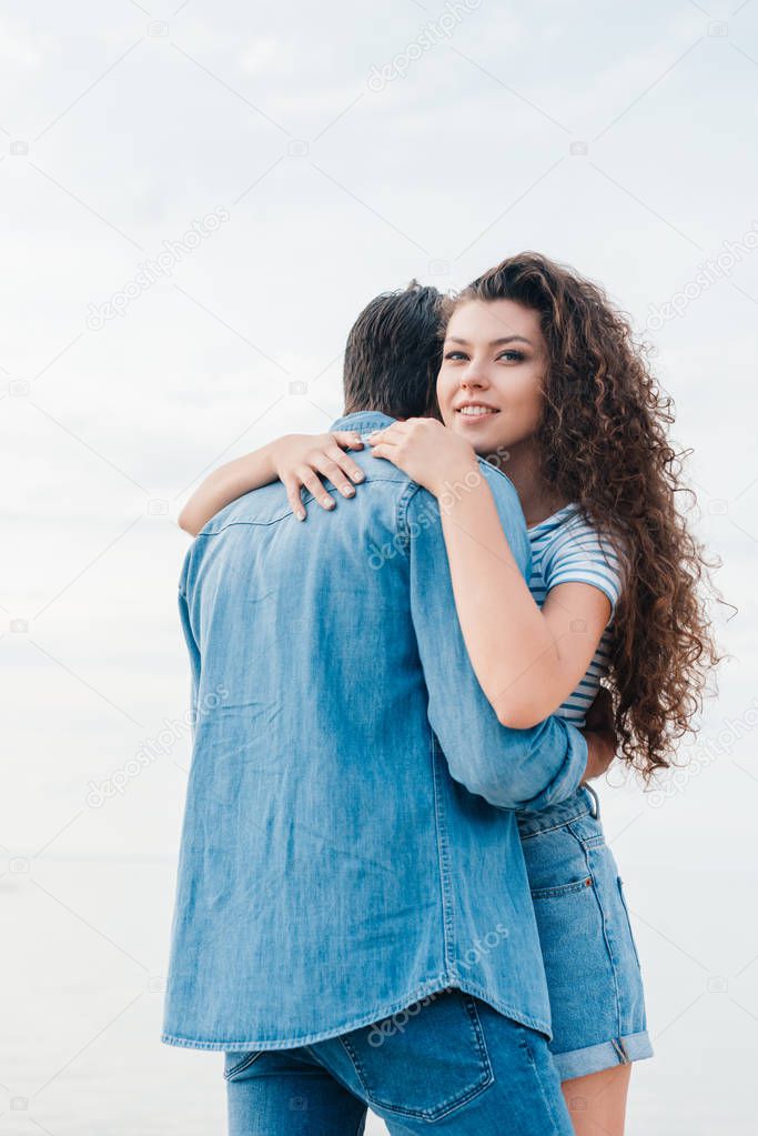 young cheerful couple hugging on beach near sea 