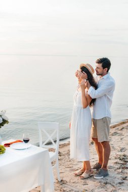 Gözlerini kapatma ve kız arkadaşı için sürpriz yapma genç adam sahilde romantik tarih