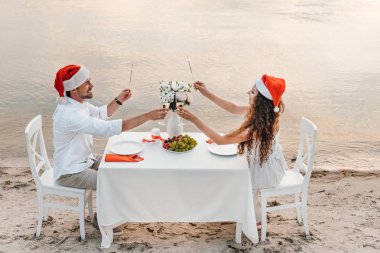 Genç çift havai fişekleri holding ve süre kutlama Noel kumsalda ile şampanya bardağı kızartma santa şapkalar