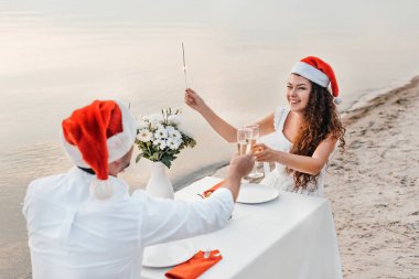 Noel kutlamaları ve plajda şampanya bardağı ile sorun Noel Baba şapkaları genç çift
