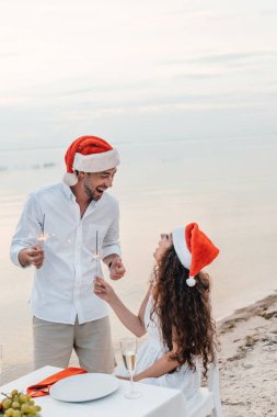 mutlu çift sahilde havai fişekleri ile kutlama Noel Noel Baba şapkaları