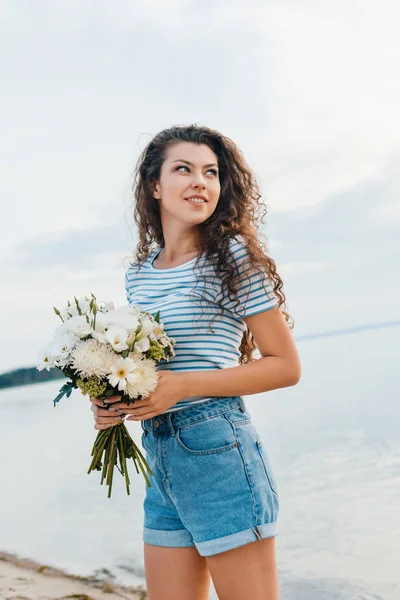 Hermosa Mujer Rizada Con Ramo Flores Posando Orilla Del Mar — Foto de stock gratis