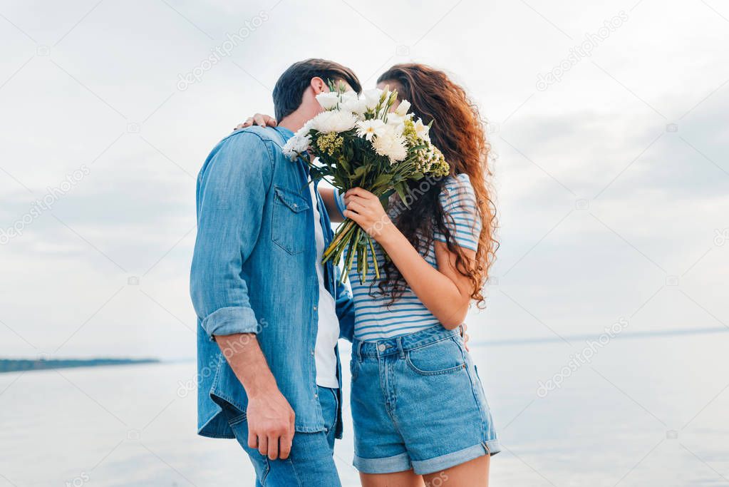 couple embracing and kissing behind the bouquet near sea 