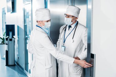 kadın doktor tıbbi maskesi Asansör ve hastane koridorda erkek meslektaşı konuşurken düğmeye 