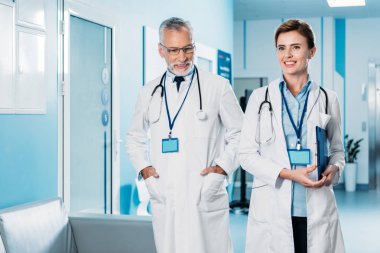mutlu kadın ve erkek doktorlarla rozetleri ve stetoskoplar hastane koridorunda yürürken boyun üzerinde 