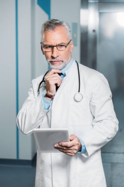 kameraya bakarak ve dijital tablet hastanede tutan boyun üzerinden stetoskop ile ciddi olgun erkek doktor 
