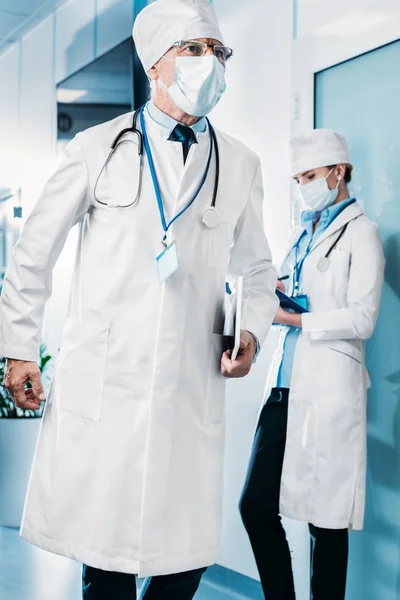 Αρσενικό Γιατρός Στην Ιατρική Μάσκα Περπάτημα Ψηφιακή Δισκίο Ενώ Συνάδελφός — Δωρεάν Φωτογραφία