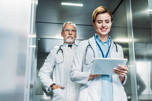 Feliz Médico Feminino Usando Tablet Digital Enquanto Seu Colega Atrás — Fotografia de Stock