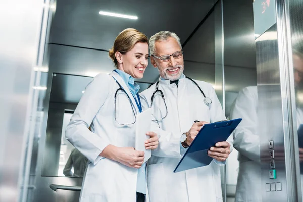 Happy Mature Male Doctor Showing Clipboard Female Colleague Digital Tablet — Stock Photo, Image