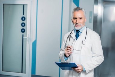 olgun erkek doktor stetoskop ile gözlük Pano ve kamera hastanede bakarak ile tutarak boyun üzerinde gülümseyen 