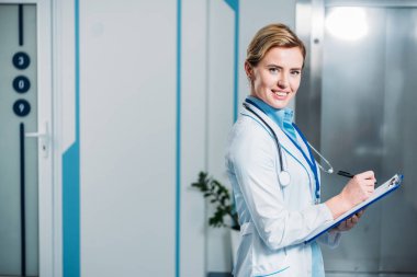 kadın doktor stetoskop ile hastane içinde clipboard yazma boyun üzerinde gülümseyen 