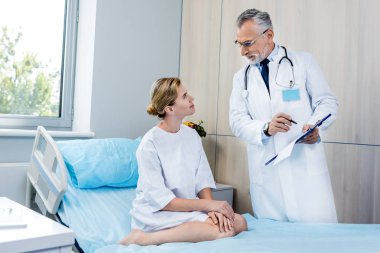 Pano bayan hasta hastane odasında işaret eden boyun üzerinden stetoskop ile erkek doktor 